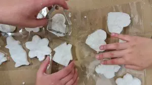 Käsiä, piparkakkumuotteja ja valkoisesta massasta muotoiltuja symboleja ylhäältä kuvattuna.