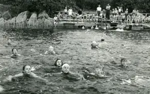 Kuvassa on lapsia uimassa vedessä. Osa katselee rannalla.