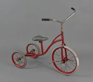 Kuvassa on lasten punainen kolmipyöräinen polkupyörä.