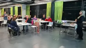 Kokoustilassa ihmisiä pienryhmäpöytien äärellä istumassa, etualalla ja taaempana tilassa seisovat naiset käyvät keskustelua toistensa kanssa.