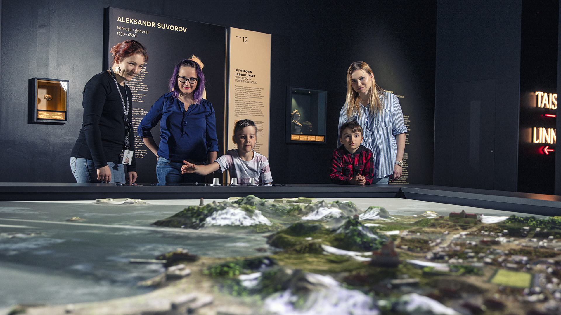 Museo-opas, lapsia sekä aikuisia kolmiulotteisen kartan äärellä näyttelyssä