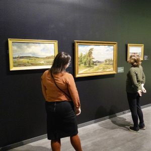 kaksi naista selkä kameraa kohti katselemassa maisemamaalauksia