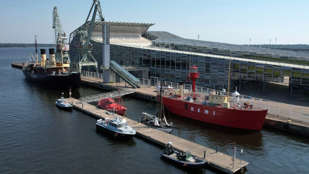 Ilmakuva Vellamon museolaiturista, jossa punaisena hohkaa majakkalaiva Kemi vierellään pienempiä aluksia ja taustallaan Vellamon rakennus